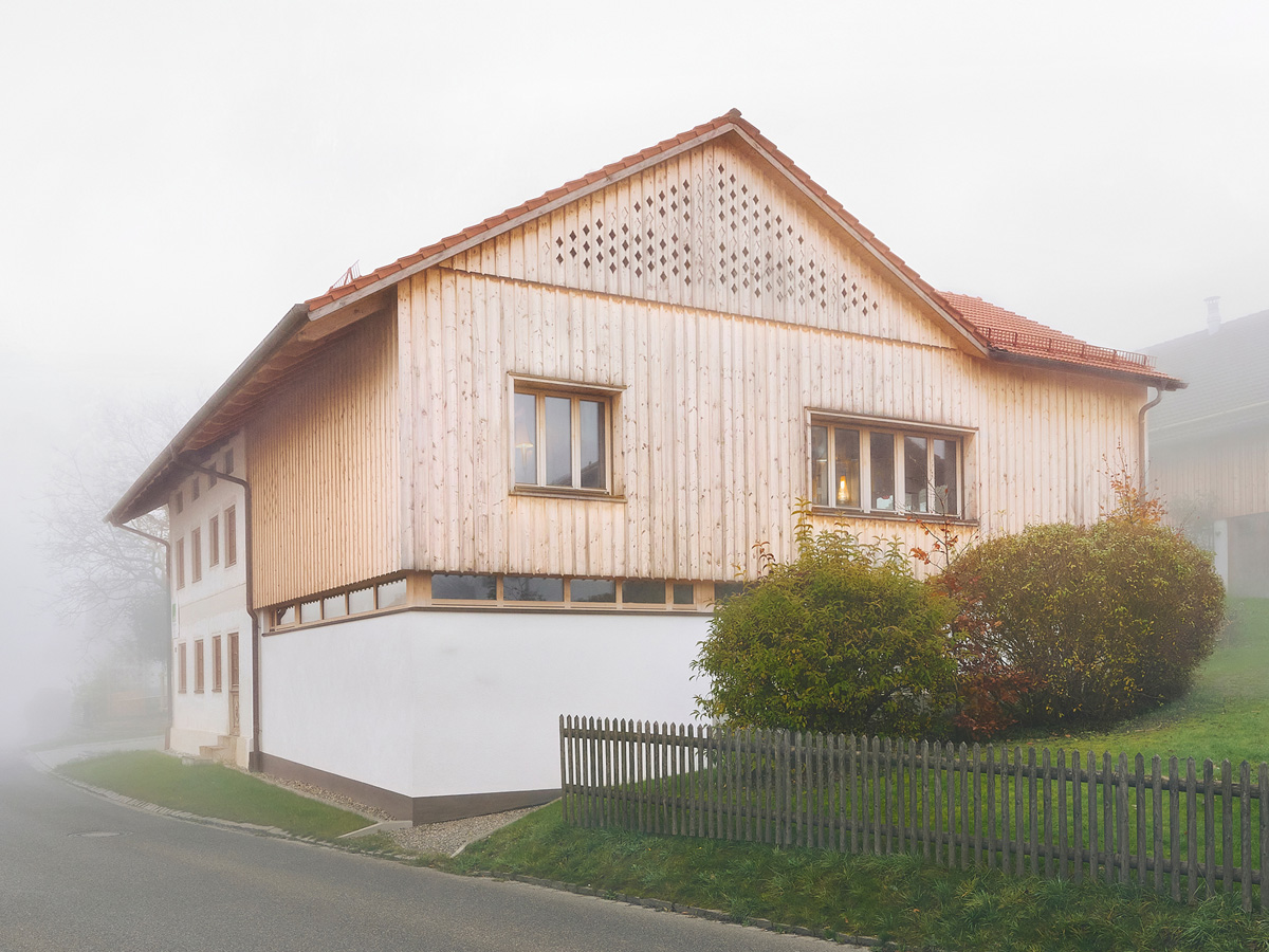 Ein zweistöckiges Haus mit Holzfassade, links ist eine Garage angebaut.