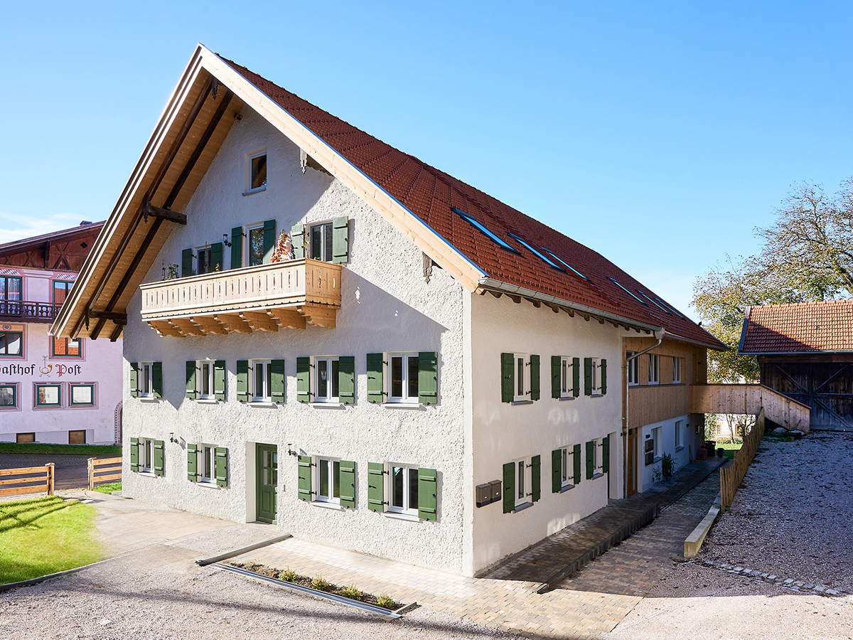 Ein zweistöckiges Haus mit Holzfassade, links ist eine Garage angebaut.