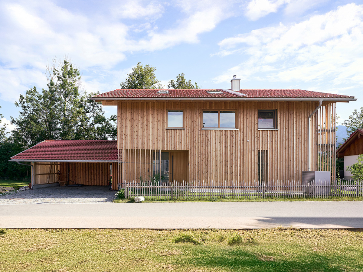 Ein zweistöckiges Haus mit Holzfassade, links ist eine Garage angebaut.