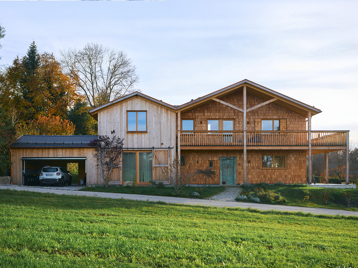 Ein zweistöckiges Haus mit Holzfassade, links ist eine Garage angebaut.