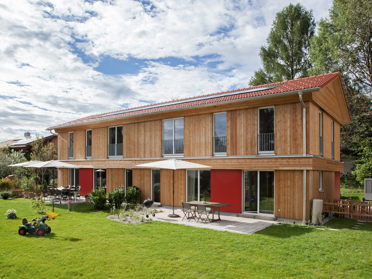 Ein zweistöckiges Haus mit Holzfassade, links ist eine Garage angebaut.
